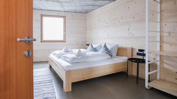 A room with a wooden bed, a small bedside table, and a window.