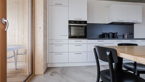 A modern kitchen with white cabinets, a built-in oven, and a wooden dining table.
