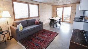 A modern living room with a grey sofa, a red patterned rug, and a dining area with a table and chairs.