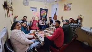 A group of people sitting around a table in a room with a ceiling fan, a guitar, and a sink. - For Rest Home Shimla  (Shimla)