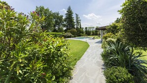 Un jardin bien entretenu, avec un chemin sinueux menant à une zone de piscine, le tout entouré d’une végétation luxuriante et de diverses plantes.