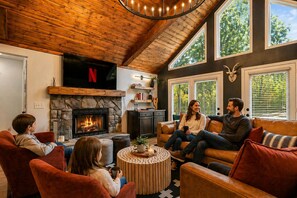 A cozy living room with a stone fireplace, leather sofas, and a Netflix sign.
