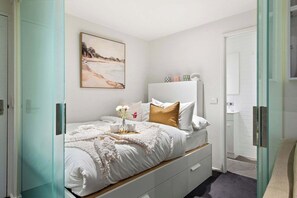 A bedroom with a bed, a bedside table, a nightstand, a wall-mounted shelf, and a painting.