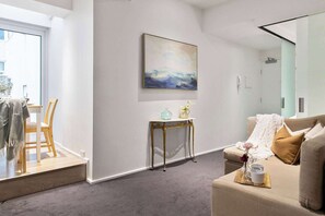 A modern living room with a sofa, a small table with a vase and two cups, and a painting on the wall. - A Cozy CBD Studio Near Melbourne Central (Melbourne)