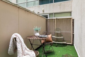 Un pequeño patio exterior con una mesa metálica redonda, una silla y una estantería decorativa de metal.