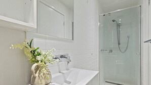 Ein modernes Badezimmer mit einem weißen Waschbecken, einer Duschkabine aus Glas und einer Blumenvase auf der Arbeitsfläche.