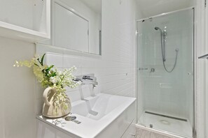 Un baño moderno con un lavabo blanco, cabina de ducha con mampara de vidrio y un florero sobre la encimera.