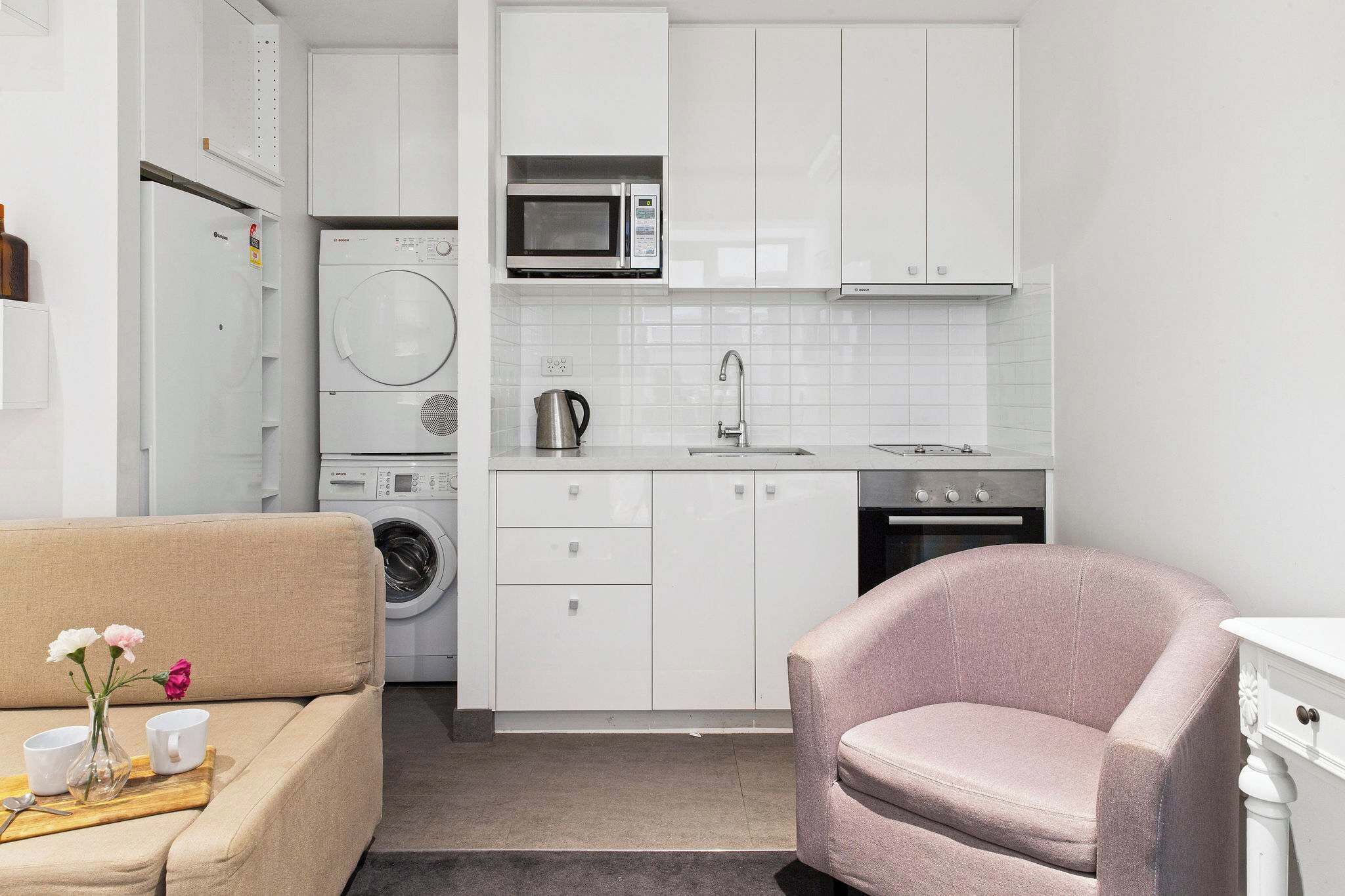 Een kleine keuken met een wasmachine, magnetron en spoelbak.