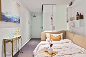 Un dormitorio ordenado con cama, mesita de noche y estante en la pared con objetos decorativos.