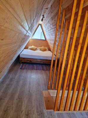 Una camera da letto mansardata accogliente, con soffitto spiovente, travi in legno e un letto con cuscini.