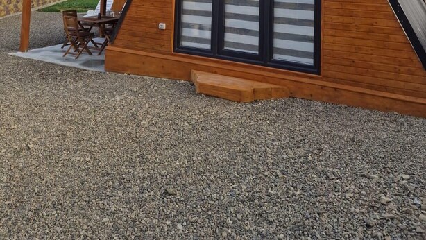 Une cabane moderne en bois, de forme triangulaire, dotée de grandes fenêtres et d’un espace patio.