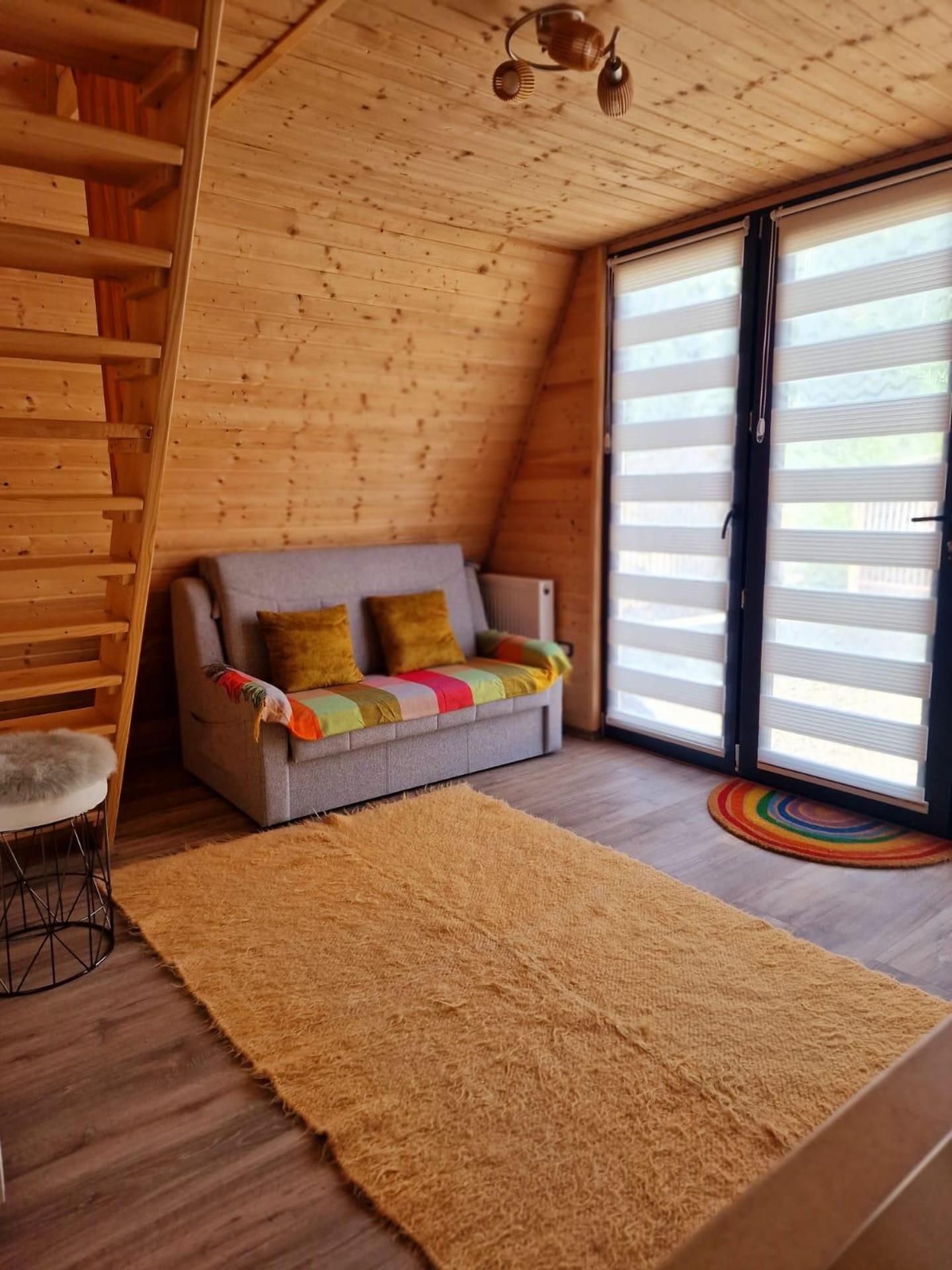 Une pièce chaleureuse avec un plafond en bois, un canapé gris agrémenté de coussins colorés, un tapis moelleux et une chaise en bois.