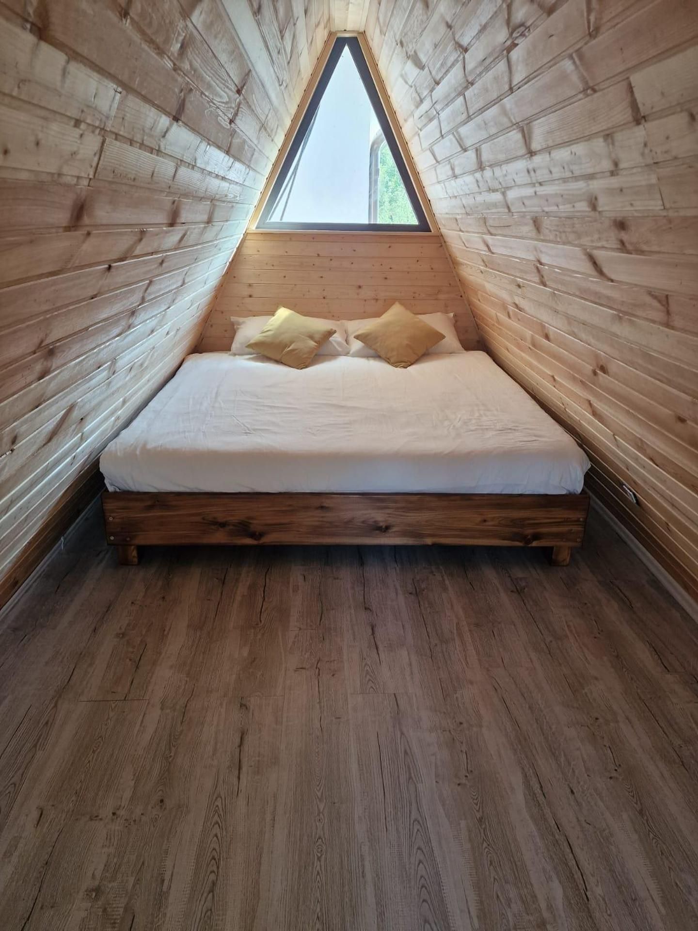 Un dormitorio abuhardillado triangular con suelo de madera y techo inclinado.