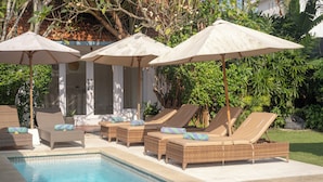 Zona de piscina con sillones reclinables y sombrillas.