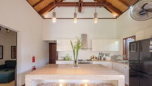 Una cocina amplia con una isla grande, taburetes de madera, luces colgantes y un refrigerador de acero inoxidable.
