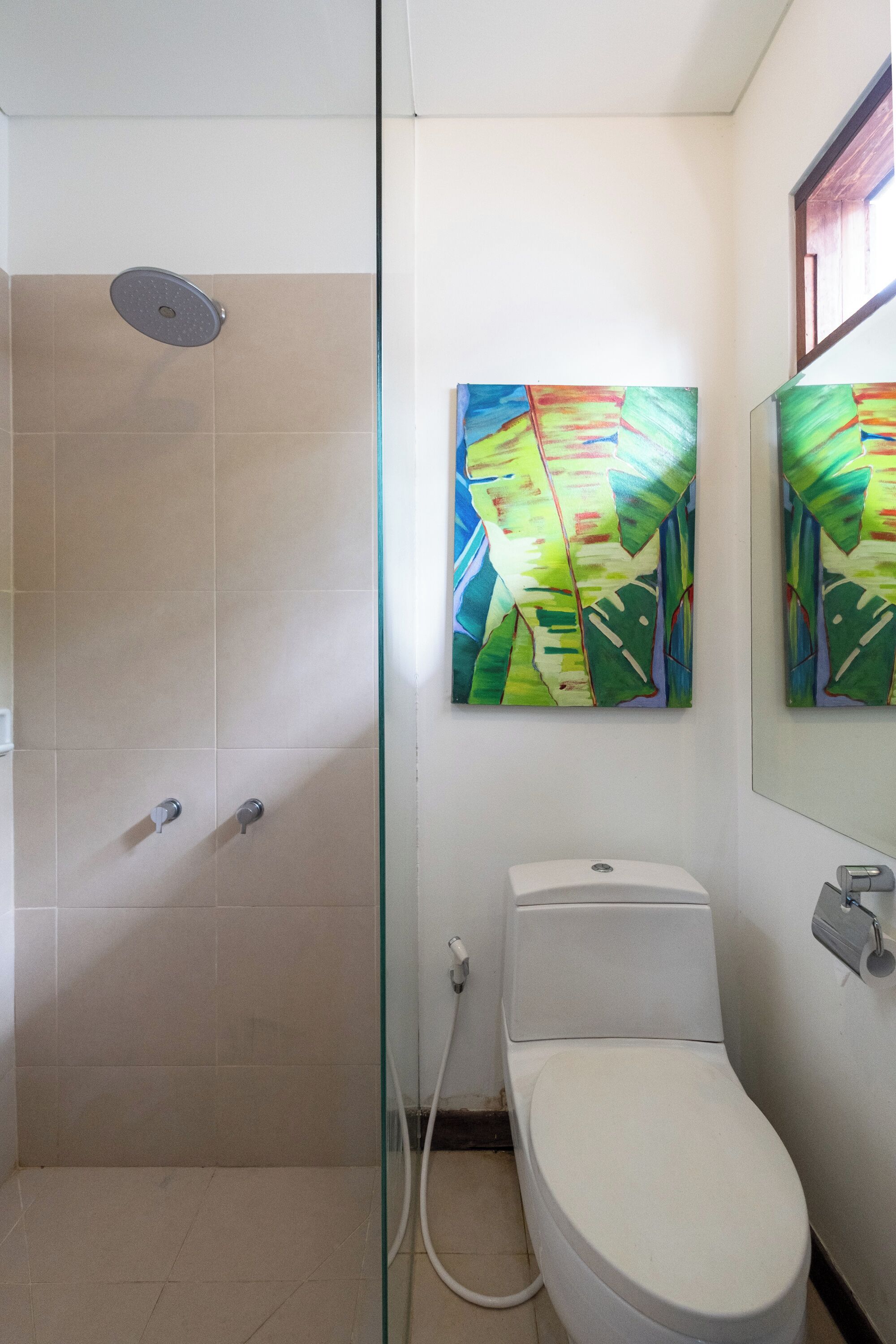 A bathroom with a shower, toilet, and two abstract paintings on the wall.