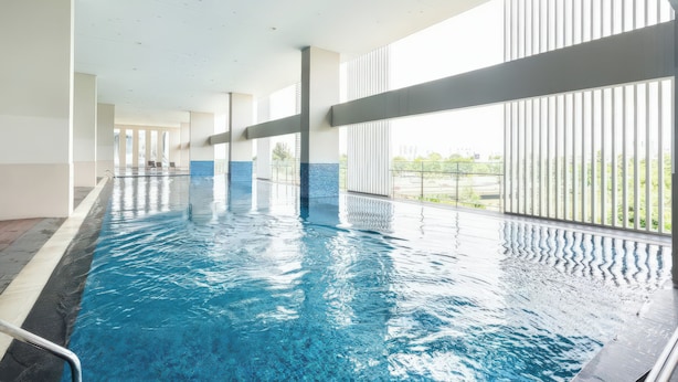 A long indoor swimming pool with clear blue water, surrounded by large windows and a tiled floor.