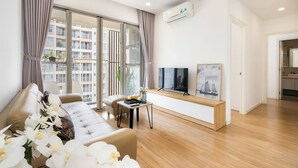 A modern living room with a sofa, a TV on a wooden console, and large windows with curtains.