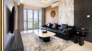 A modern living room with a black leather sofa, a marble wall, and a large window offering a city view.