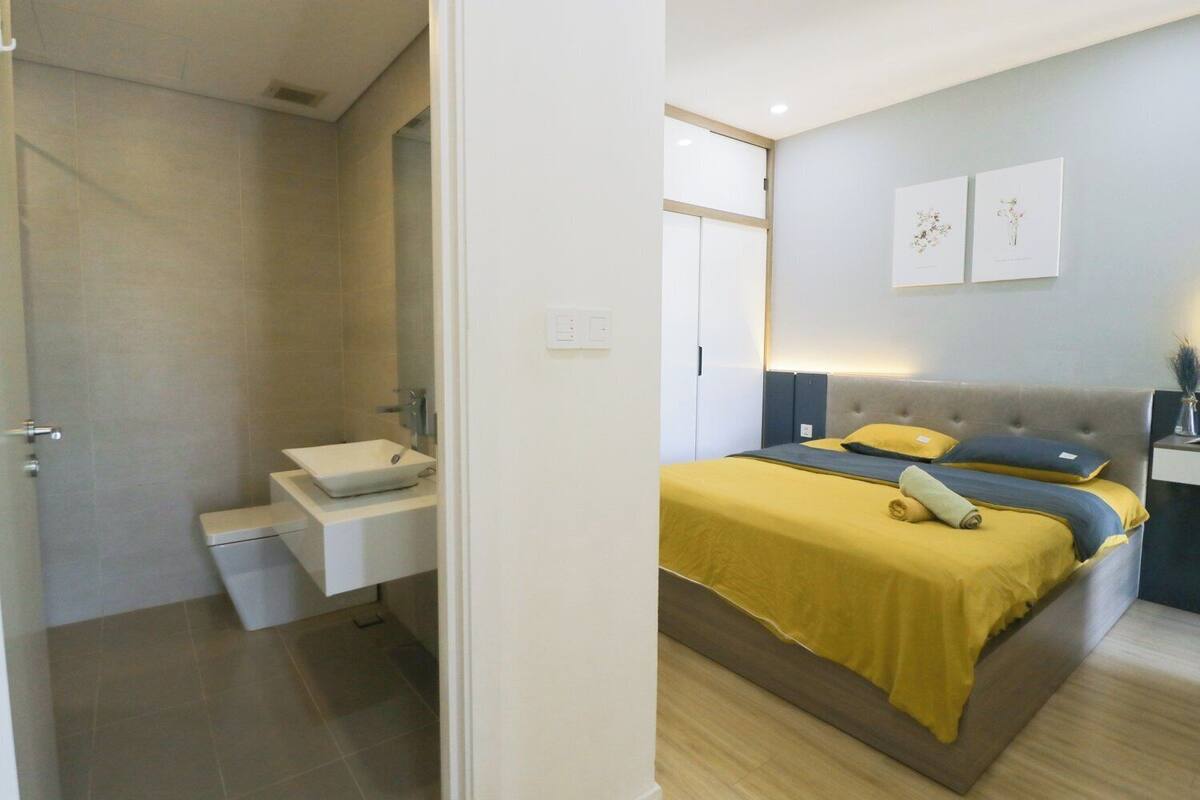 A bedroom with a bed, bedside table, and a bathroom with a sink and toilet.