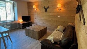 Ein gemütliches Wohnzimmer mit einer Holzwand, einem Ledersofa, einem Fernseher und einem kleinen Tisch.