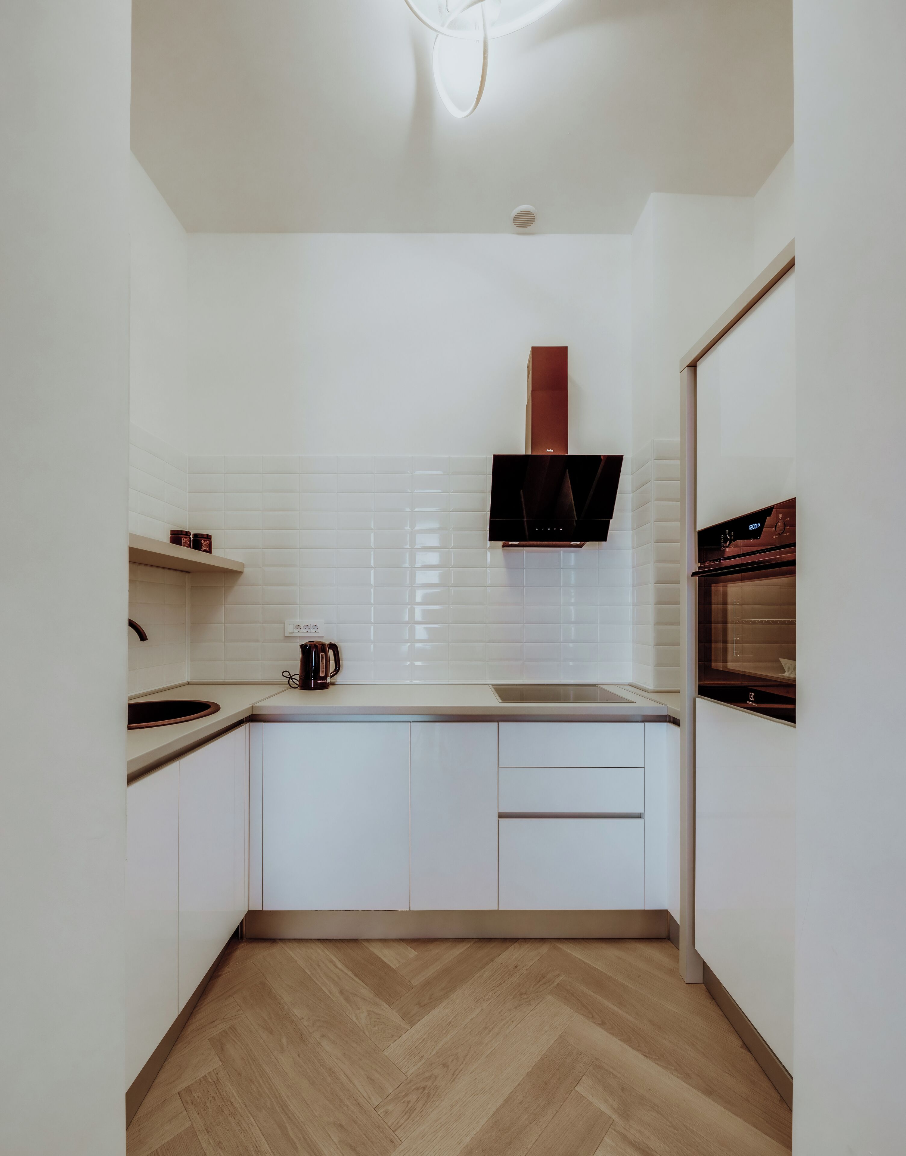 Una cucina moderna con mobili bianchi, pavimento in legno a spina di pesce, forno integrato e microonde a parete.