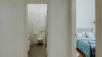 A hallway leading to a bathroom with a toilet and a shower.