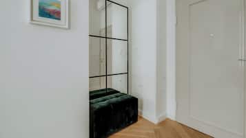 A hallway with a wooden floor, a black-framed mirror, a green cushioned bench, and a white door.