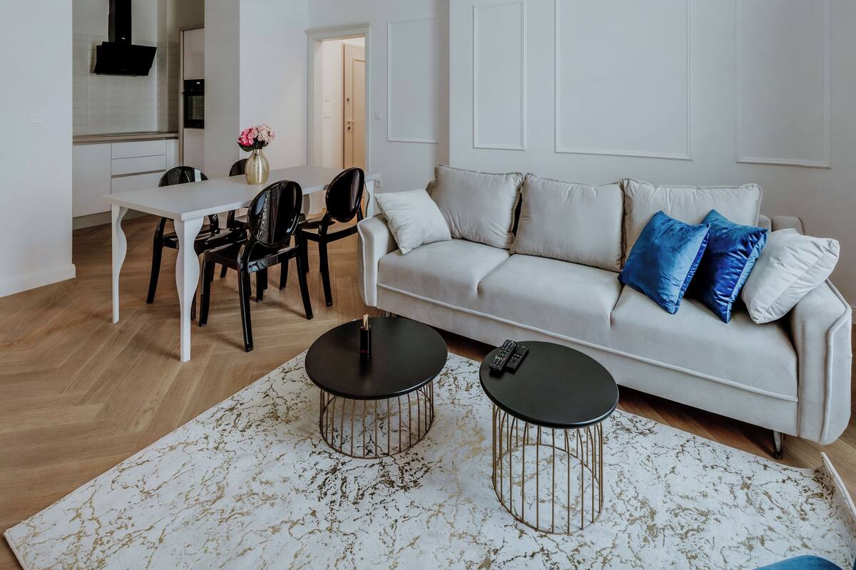Un salon moderne avec un canapé blanc, deux tables basses noires et un tapis blanc à motifs.
