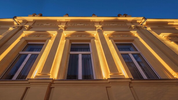 A classical building facade with symmetrical columns and large windows, illuminated by warm lighting. - LAVilla Osijek (Osijek)