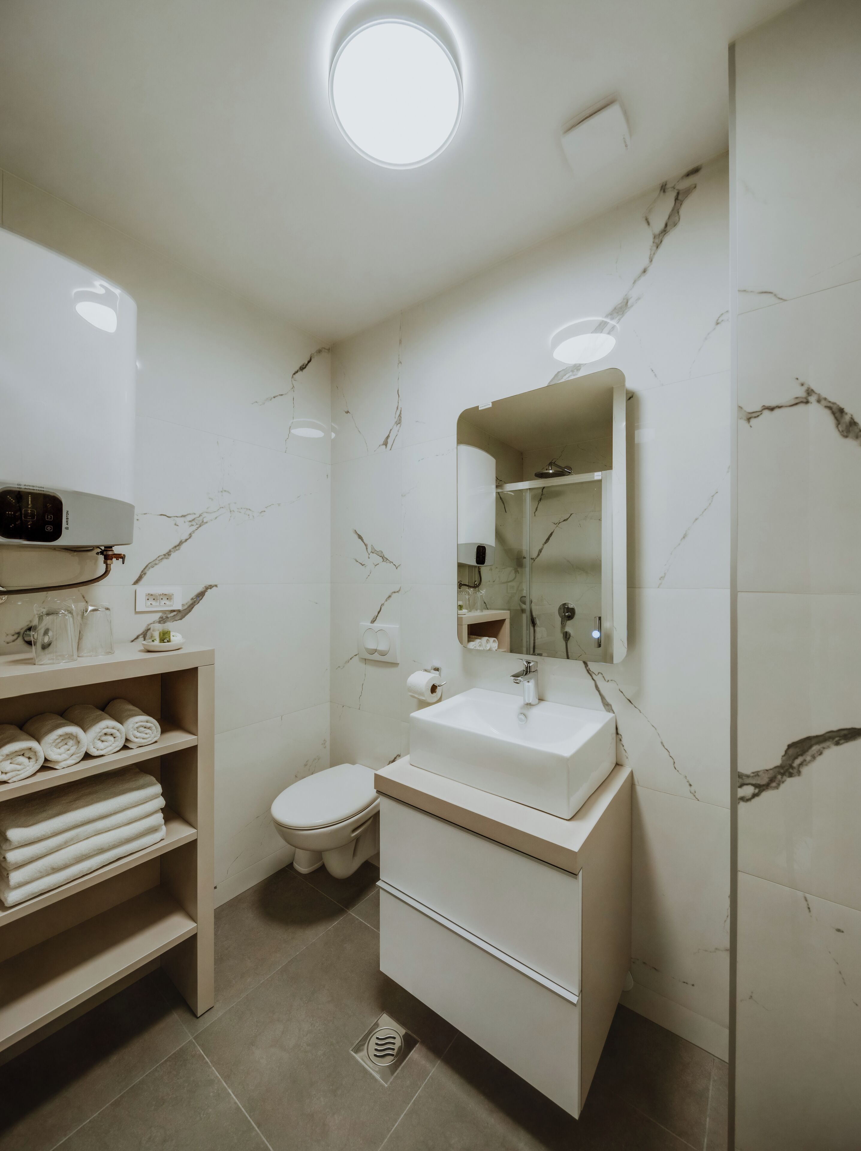 Un baño moderno con una salpicadura de mármol blanco, un lavamanos empotrado, un inodoro y un estante con toallas.