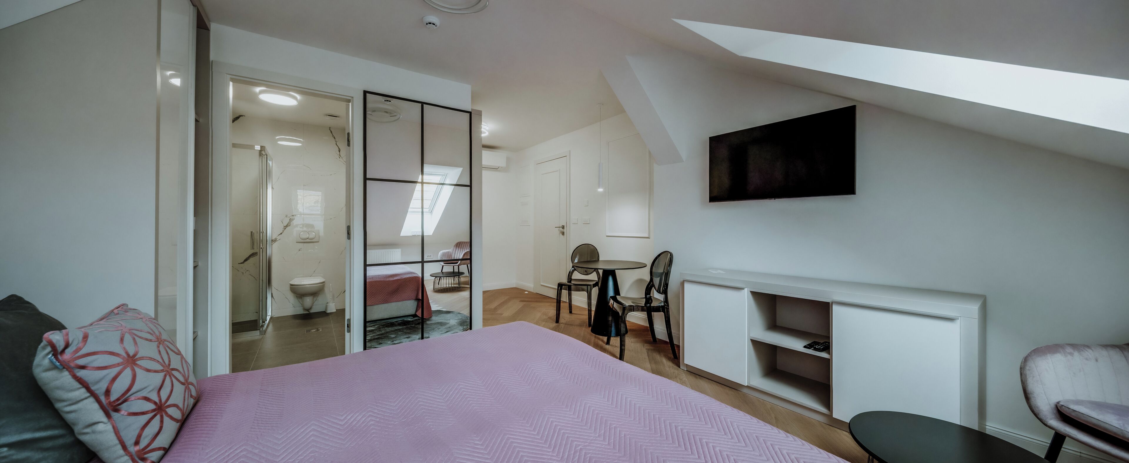 A bedroom with a bed, a TV mounted on the wall, a fireplace, and a small dining area.