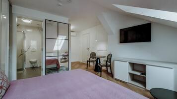 A bedroom with a bed, a TV mounted on the wall, a fireplace, and a small dining area.