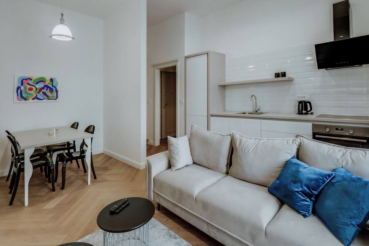Un salon moderne comprenant un canapé, une table à manger et des chaises. Il y a également un coin cuisine avec une télévision et une machine à café.