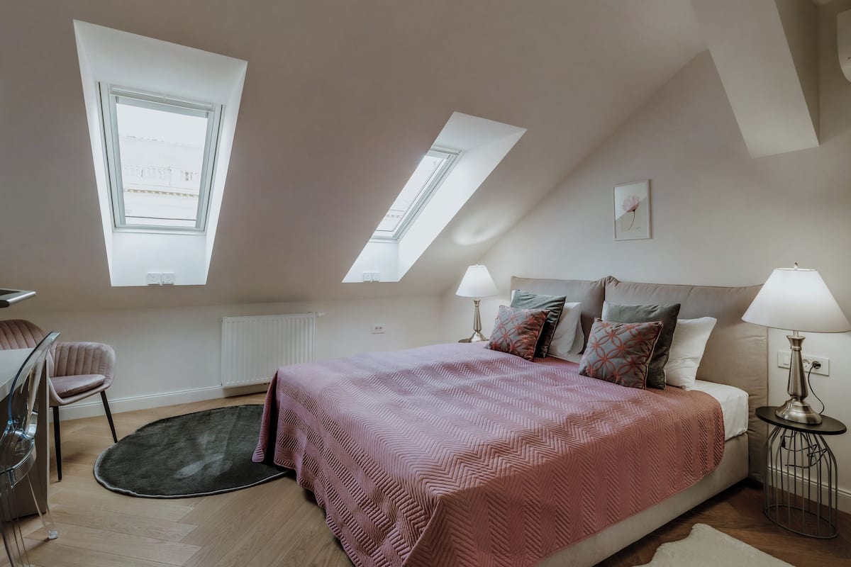 Une chambre à coucher avec un grand lit, des fenêtres de toit, une chaise, une table et un radiateur.