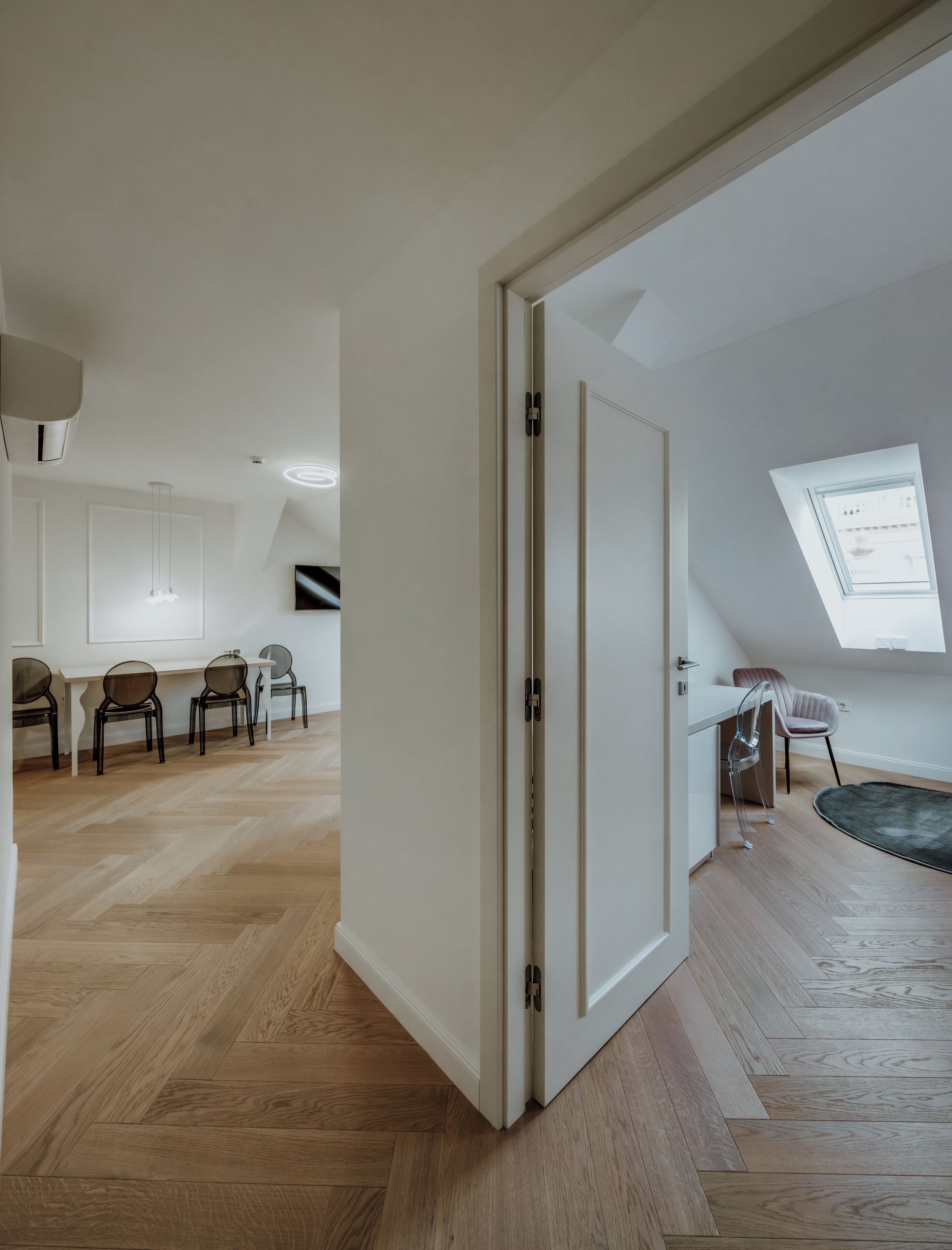 A spacious room with a wooden herringbone floor, a white door, and a skylight.