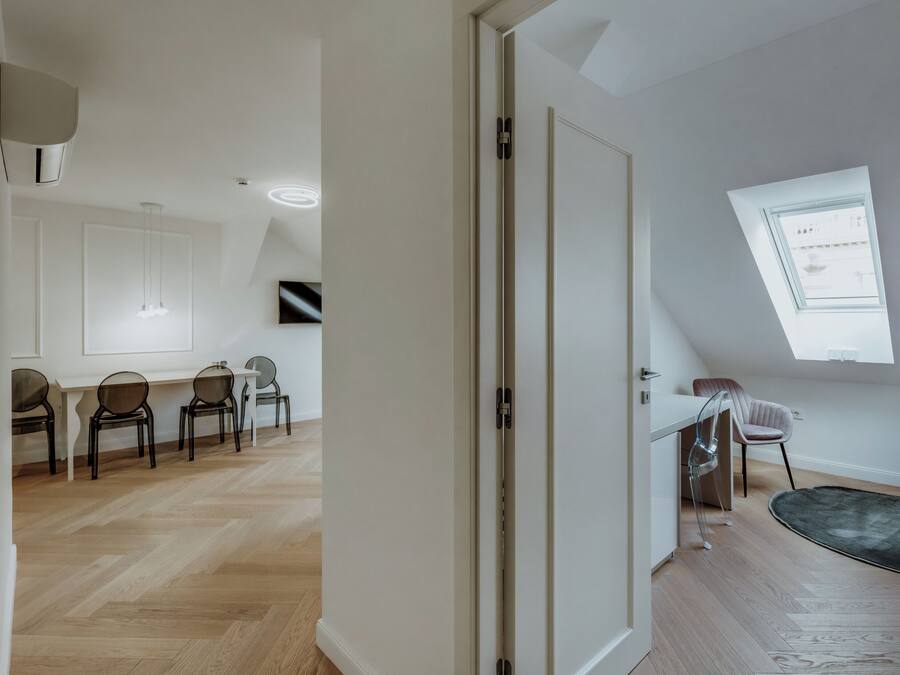 A spacious room with a wooden herringbone floor, a white door, and a skylight.