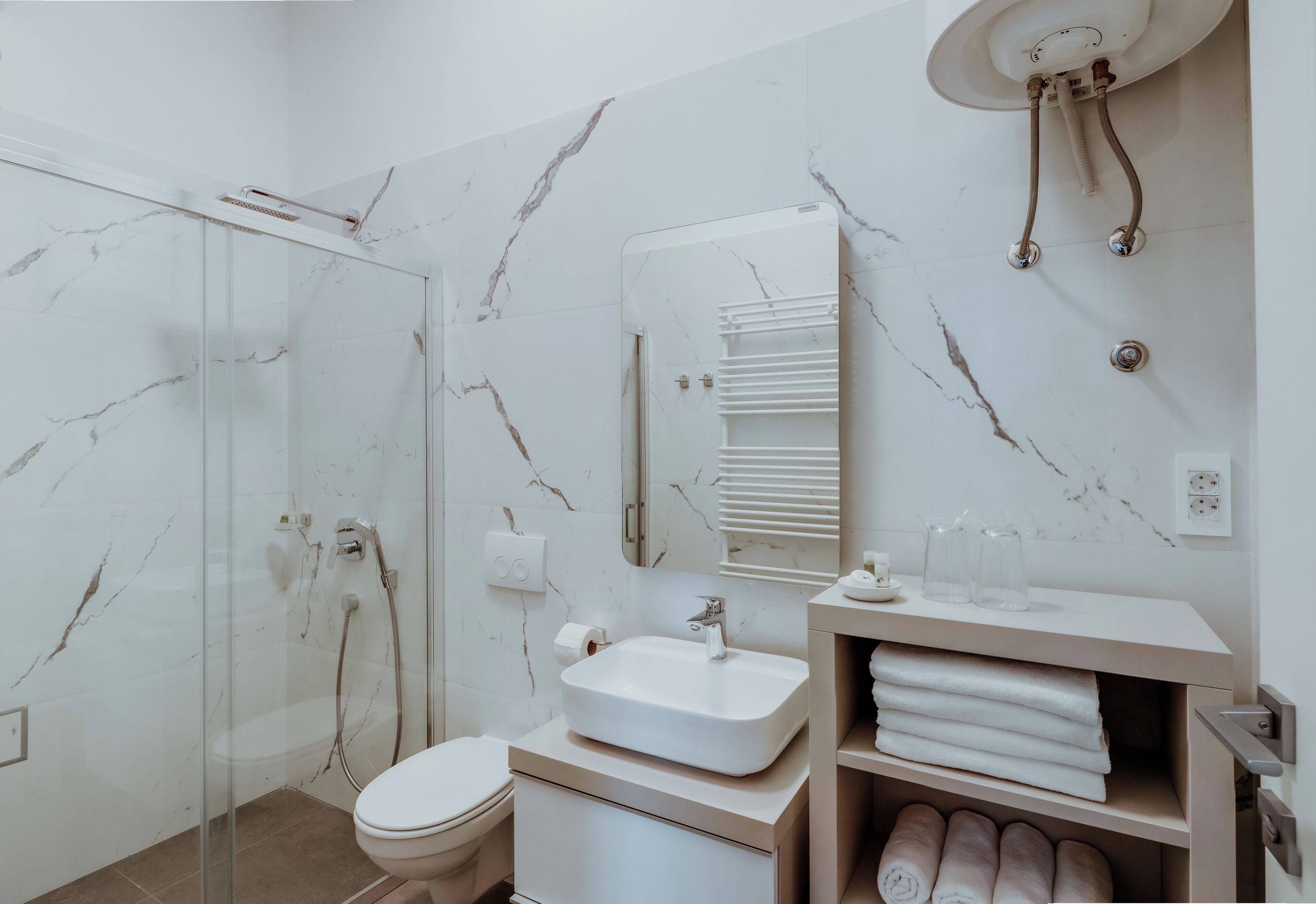 A modern bathroom with a glass-enclosed shower, a white sink, a mirror, and a towel rack.