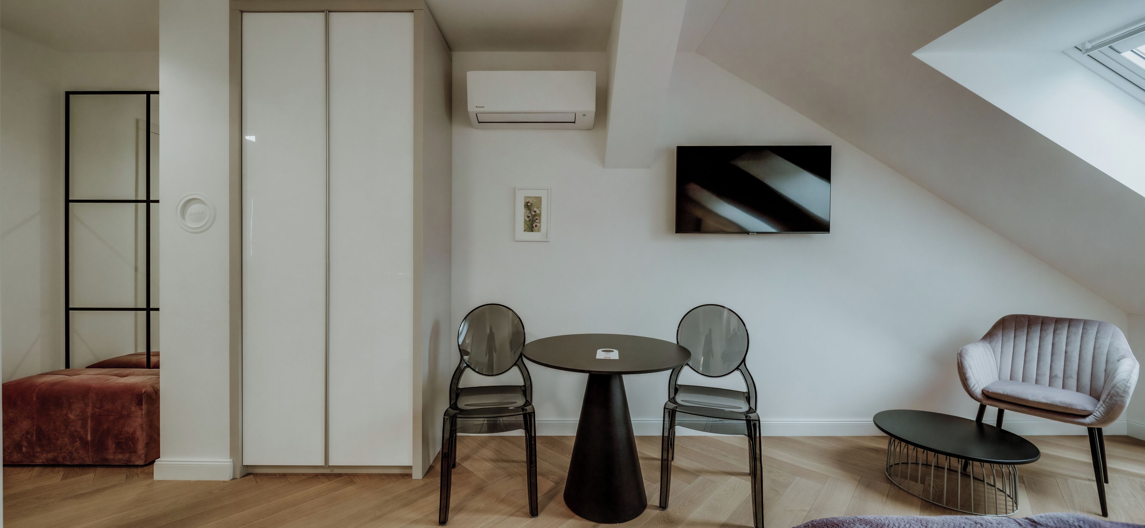 A modern living room with a sofa, two chairs, a small table, and a TV on the wall.
