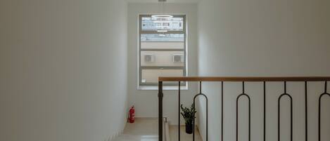 Una escalera que lleva a una plataforma con una ventana, un extintor y una planta en maceta.