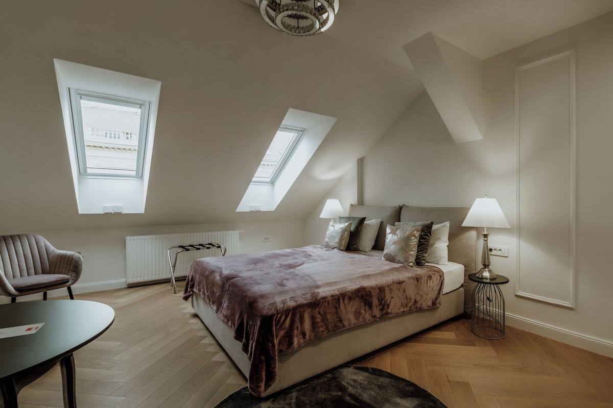 Une chambre à coucher avec un lit, une chaise, une table et une lampe. Il y a des fenêtres de toit et un radiateur.