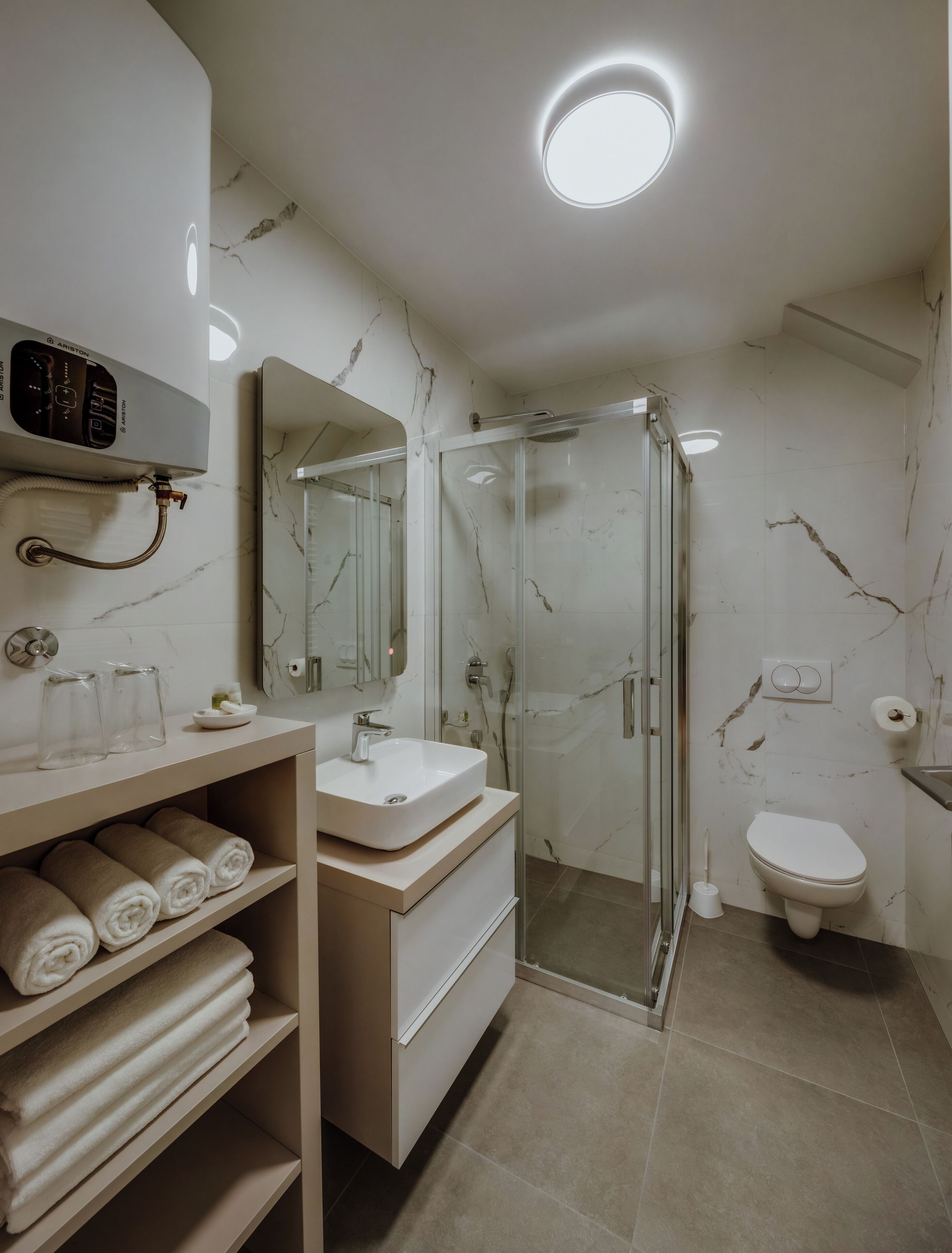 Un baño moderno con ducha de vidrio, un lavamanos blanco y un inodoro.