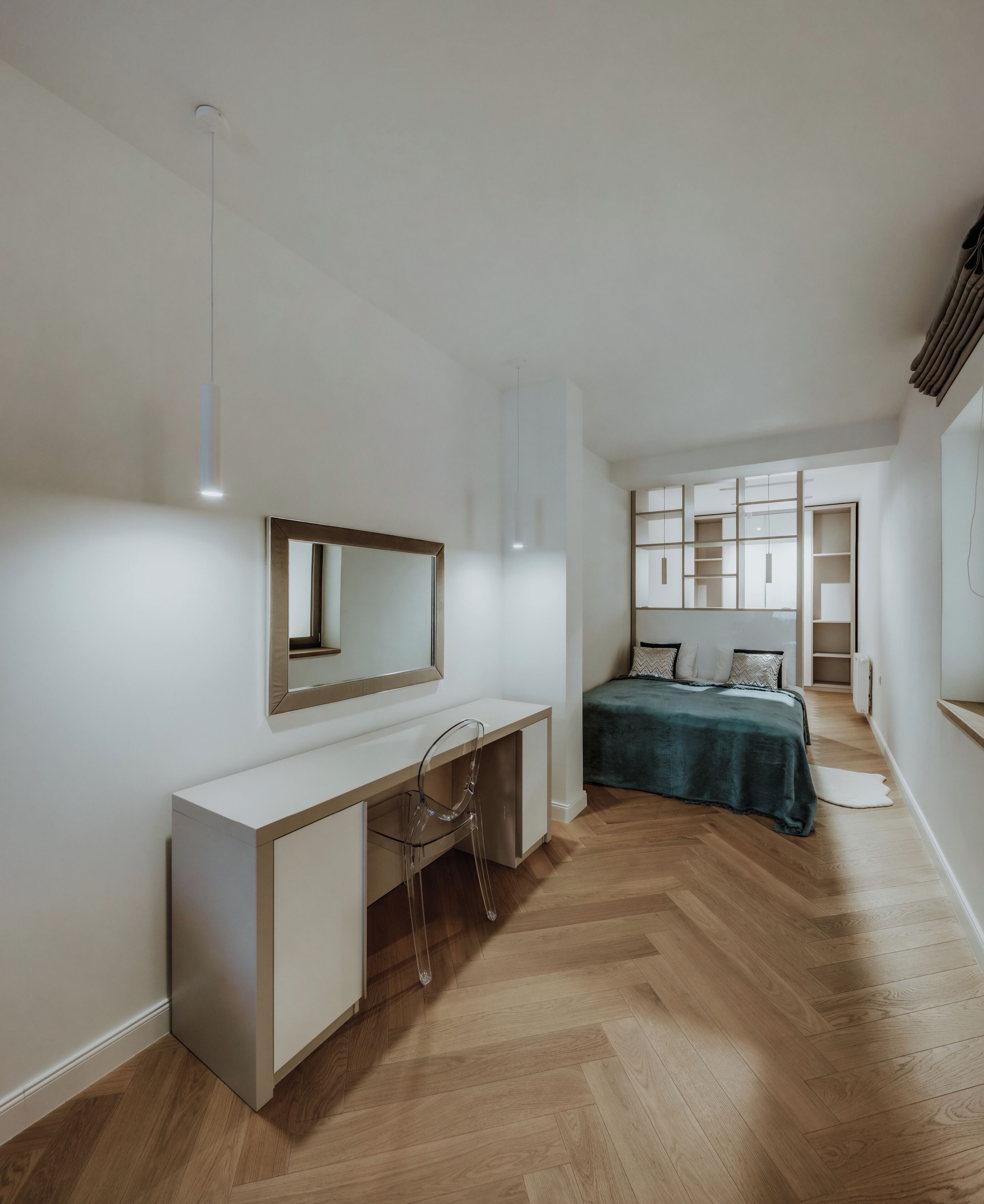 Een moderne slaapkamer met een houten vloer, een wit bureau met stoel, een bed met groene deken en een groot raam met planken.