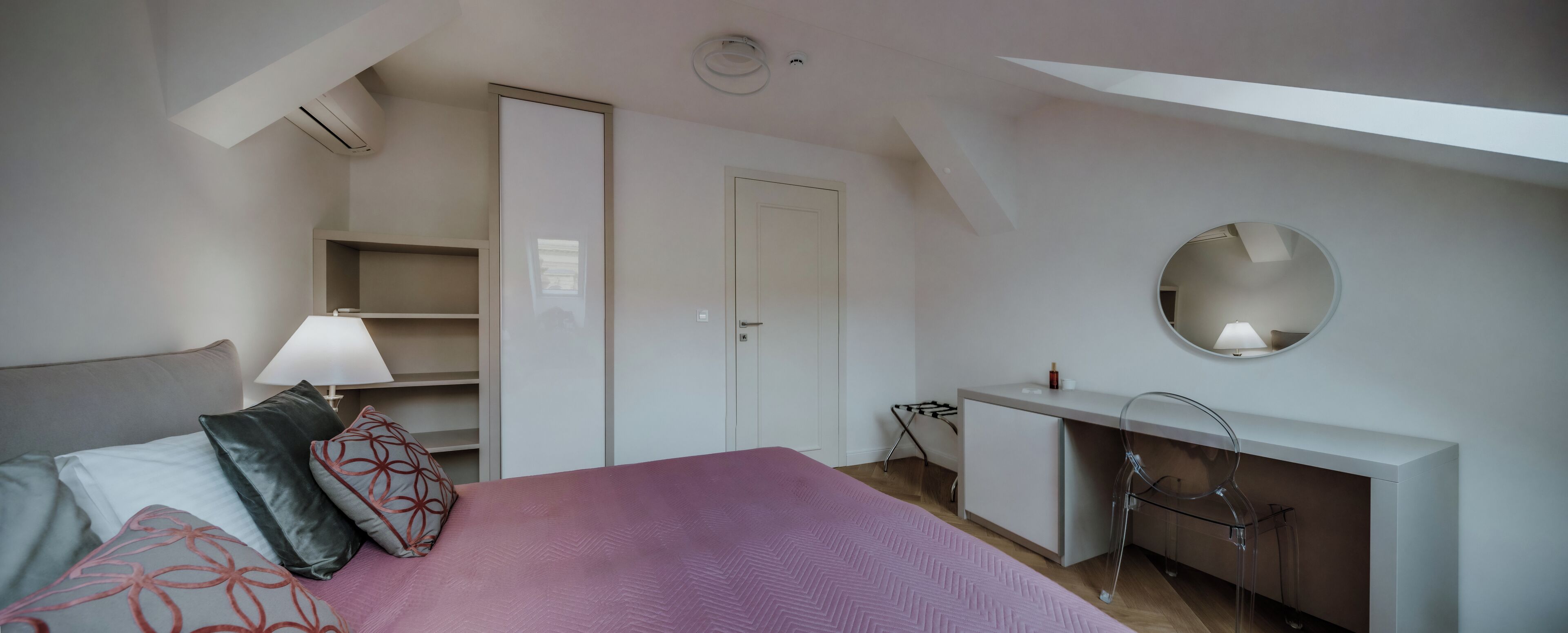 A bedroom with a bed, a desk, a mirror, and a wardrobe.