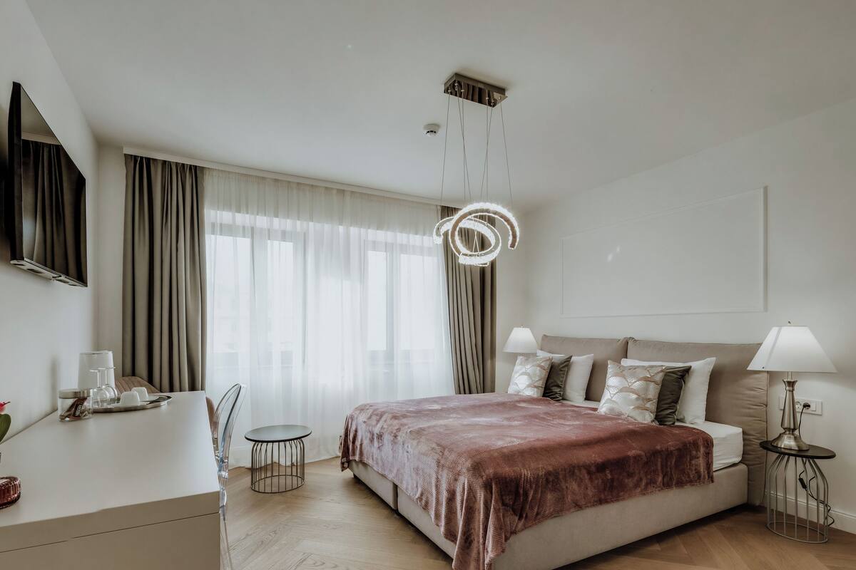 Une chambre d’hôtel moderne équipée d’un lit, de tables de chevet, d’un bureau et d’une grande fenêtre avec des rideaux.