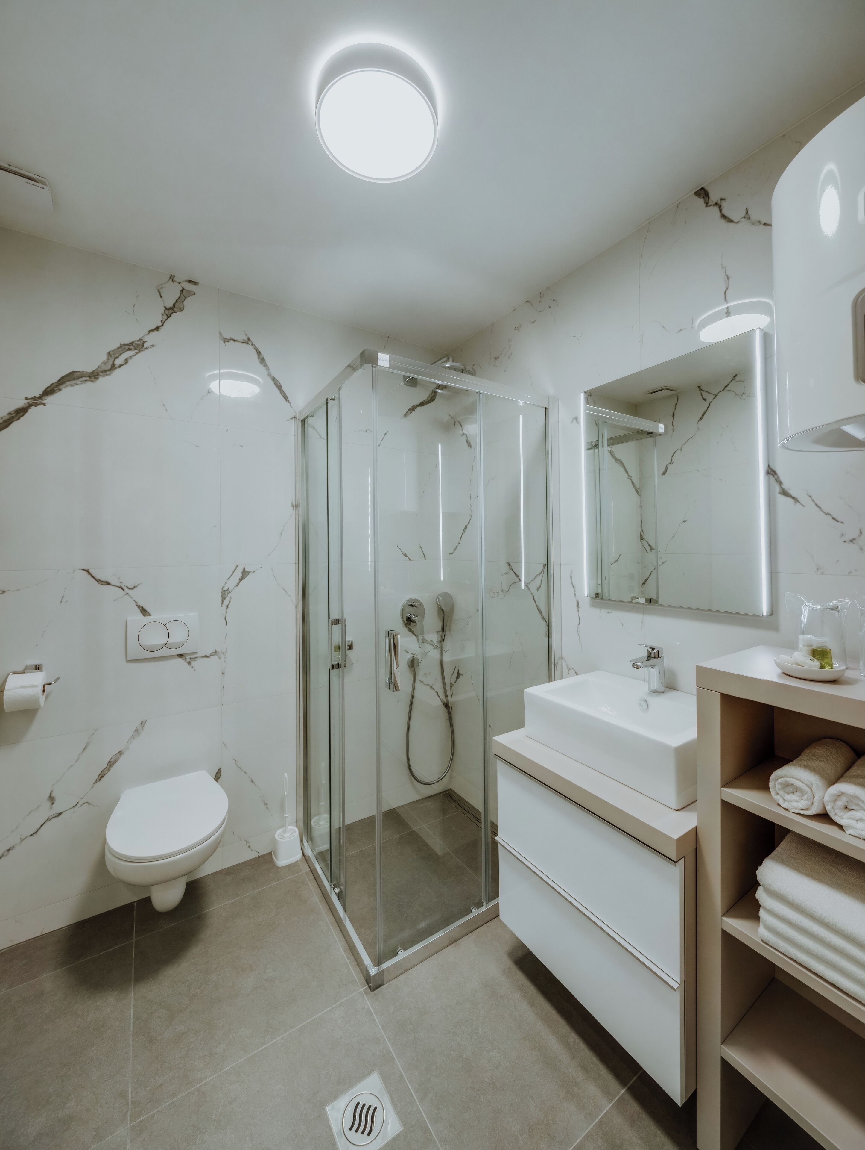 A modern bathroom with a glass-enclosed shower, a toilet, a sink, and a vanity with towels.