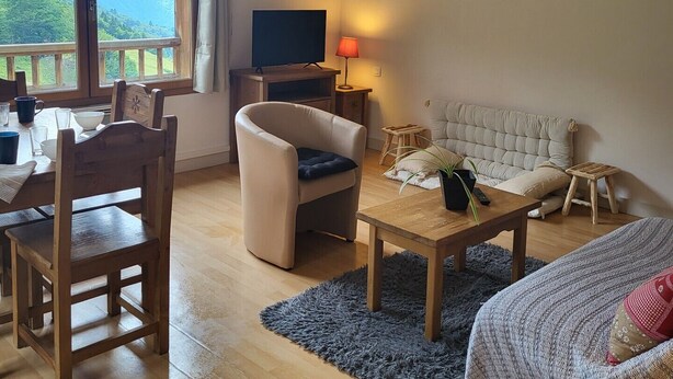 A living room with a sofa, a TV, a dining table with chairs, and a view of mountains through large windows.