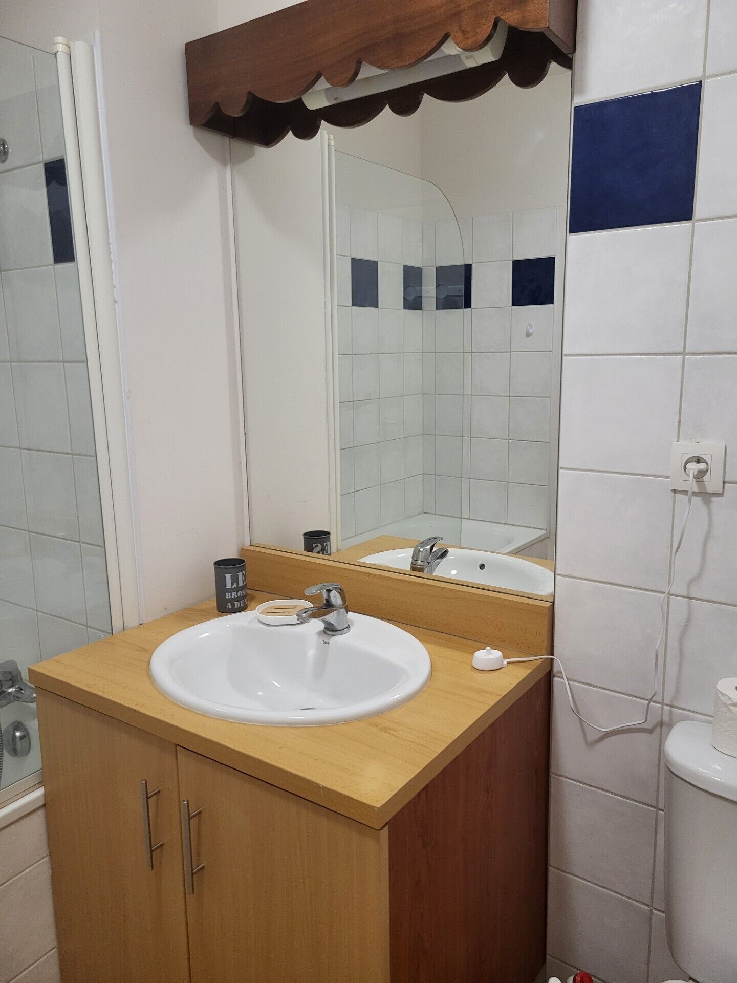 A bathroom with a wooden vanity, a white sink, a mirror, and a toilet.