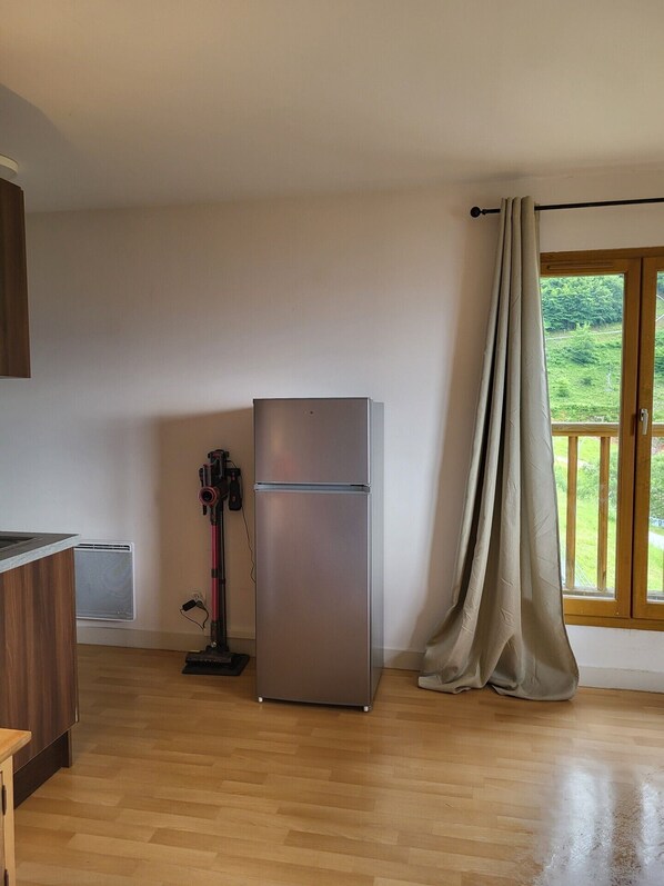 Una cocina con un refrigerador de acero inoxidable, un armario de madera y una ventana con cortina.