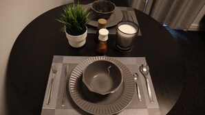 Une table à manger dressée avec une assiette, un bol, des couverts, une bougie, une petite plante et un salier et un poivrier.